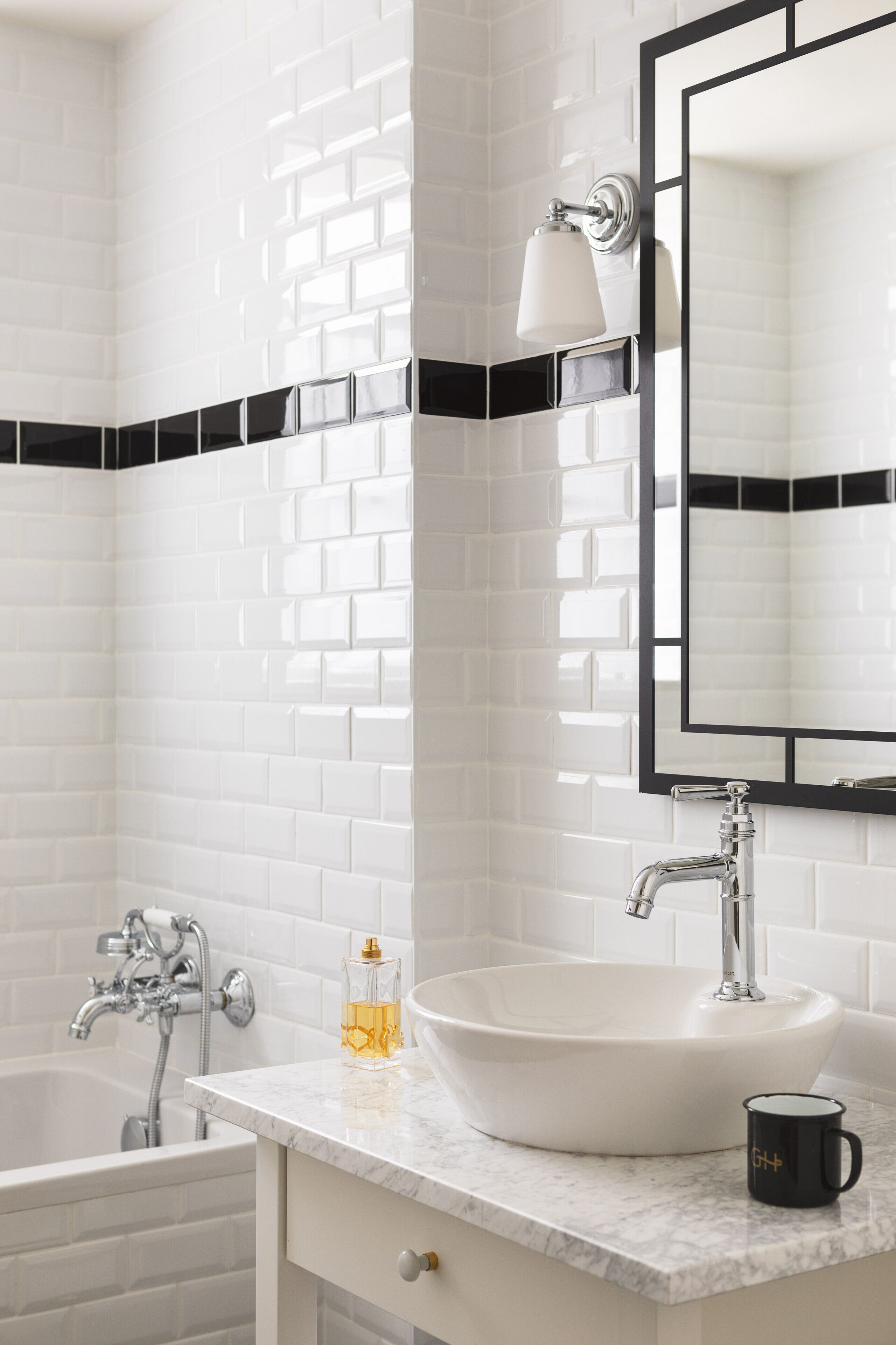 A bathroom with white subway tiles, a white sink, a black and white towel rack, and a black-framed mirror.