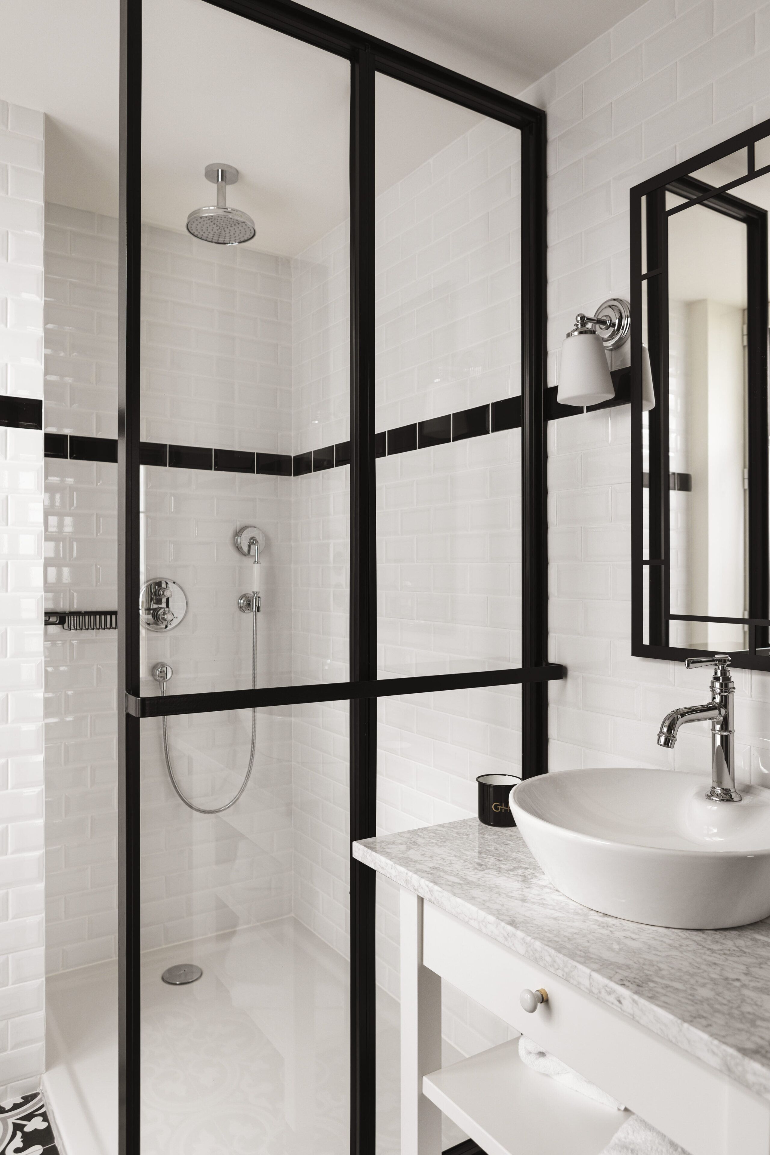 A modern bathroom with a glass-enclosed shower, a white sink, and a black-framed mirror.