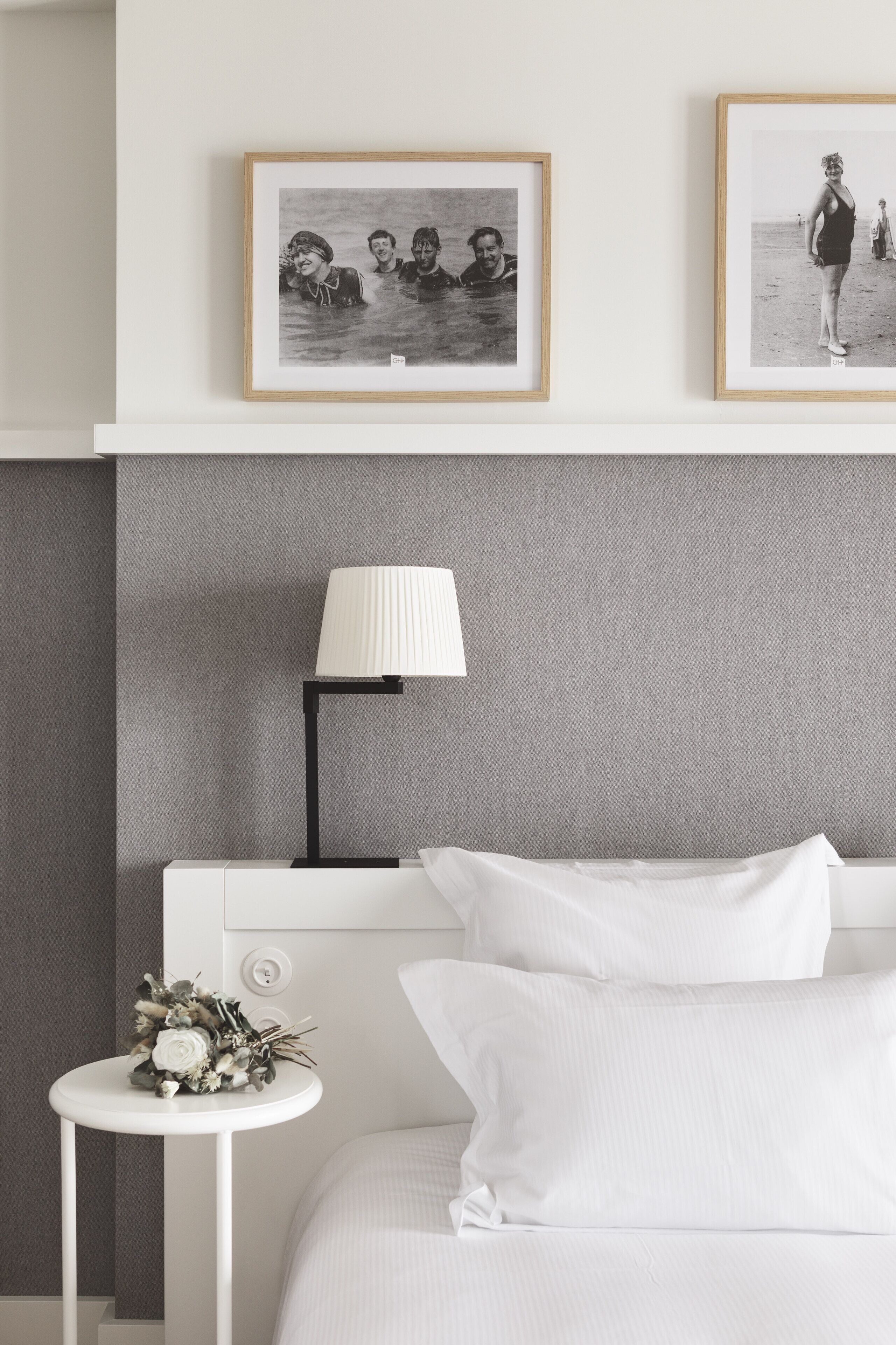 Un dormitorio ordenado con una cama, una mesita de noche con lámpara y dos fotografías enmarcadas en la pared.