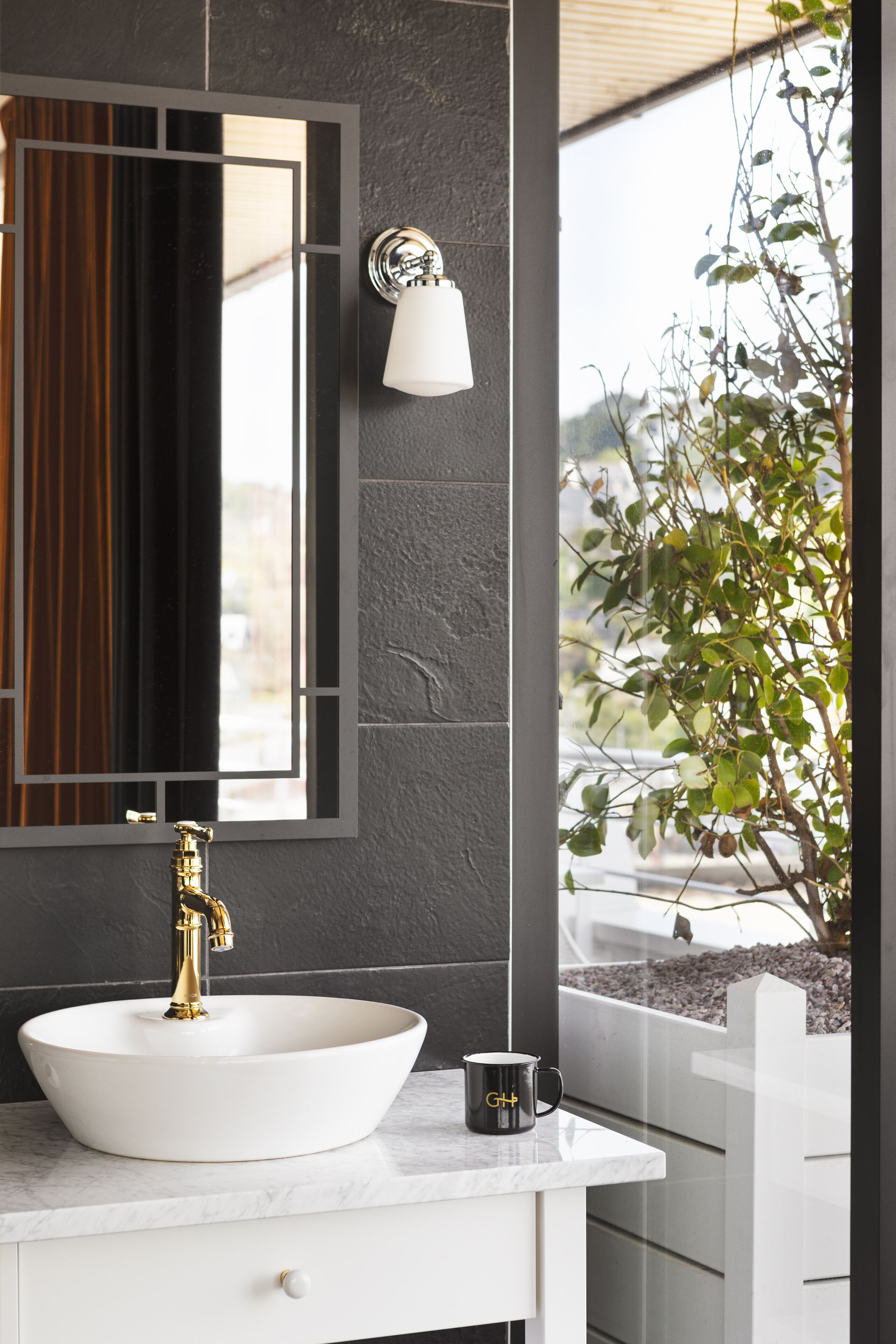 Une salle de bain avec un lavabo blanc, un robinet doré et un miroir avec un cadre noir.