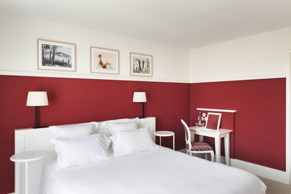 A hotel room with a large bed, two bedside tables, a desk with a chair, and three framed pictures on the wall.