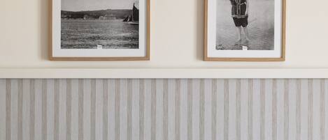 A hotel room with a bed, a bedside table with a book and a pair of scissors, and two framed black and white photographs on the wall.