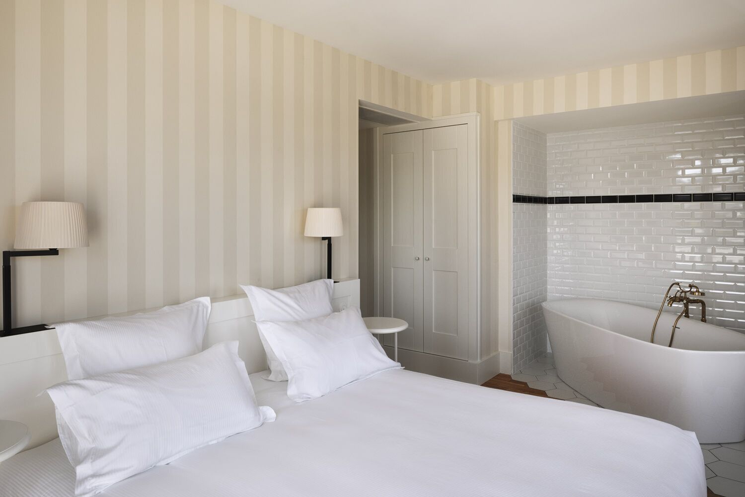 Una habitación de hotel con una cama grande, una bañera blanca y una pared a rayas.