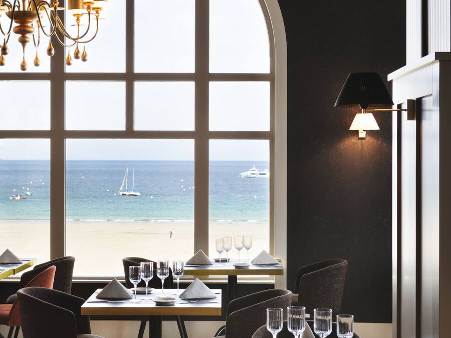 A dining area with a large window overlooking a beach, a chandelier, and a table set for four.