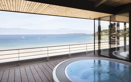 A modern balcony with a wooden floor, a glass railing, and a view of the sea.