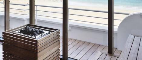 A modern room with large windows overlooking a beach, a wooden deck, and a built-in fireplace.