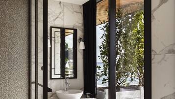 A modern bathroom with a white marble sink, a large mirror, and a view of the outdoors through a glass door.