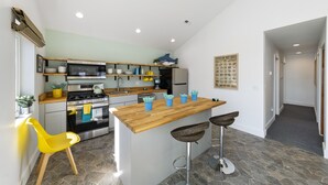 Une cuisine moderne avec un îlot central, des tabourets de bar et une chaise jaune.