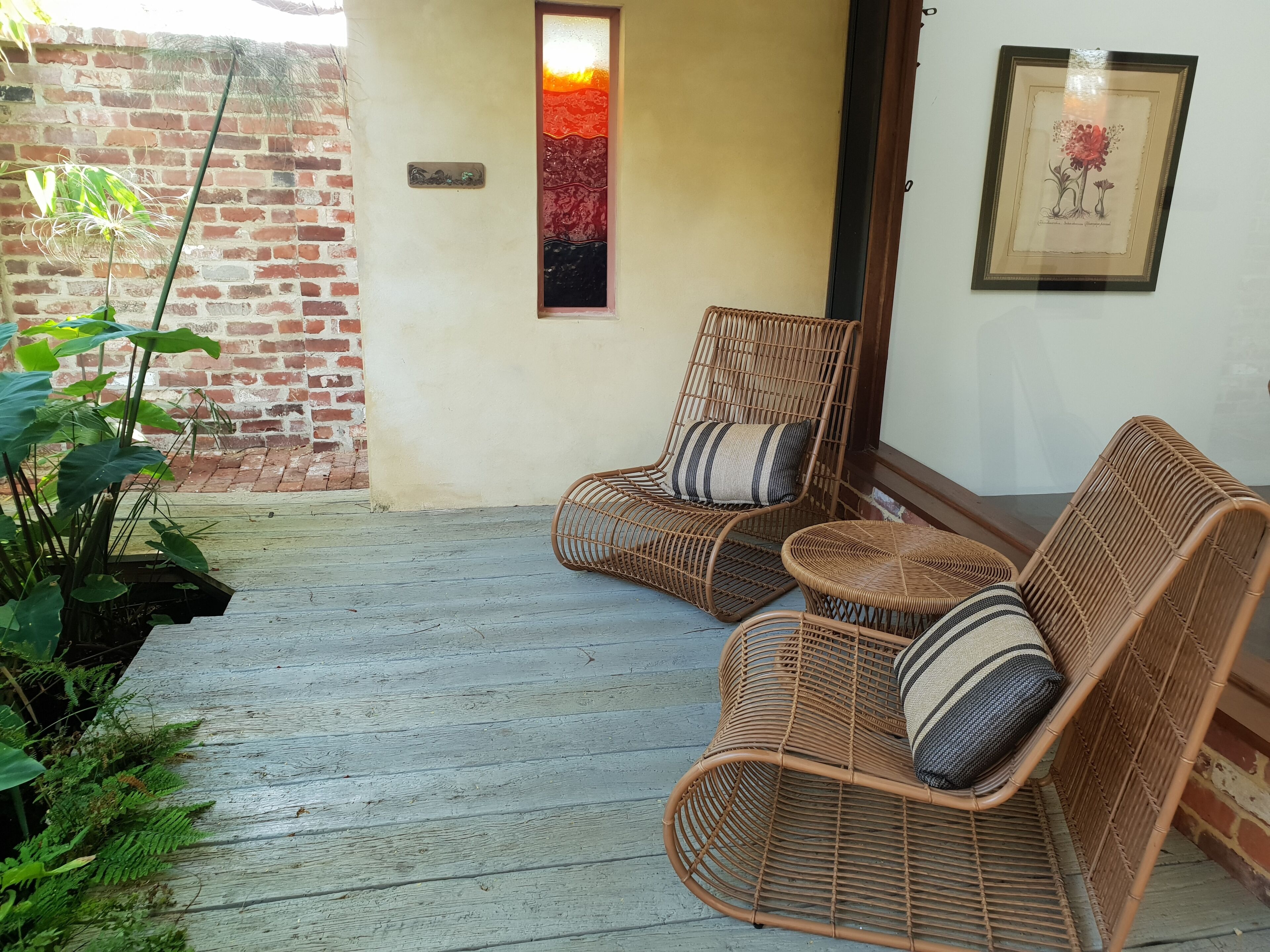 A wicker chair with a cushion and a small round table, both placed on a wooden deck.