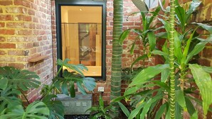 Pared de ladrillo con una ventana, plantas en macetas y un estante pequeño.