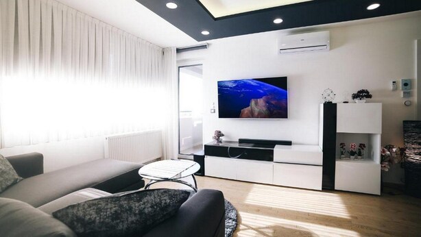 Un salon moderne comprenant un canapé, une table basse, un téléviseur à écran plat fixé au mur et un meuble de rangement blanc avec des étagères.