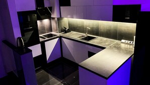 Une cuisine moderne avec un plan de travail noir, des appareils en acier inoxydable et un éclairage d’ambiance violet.