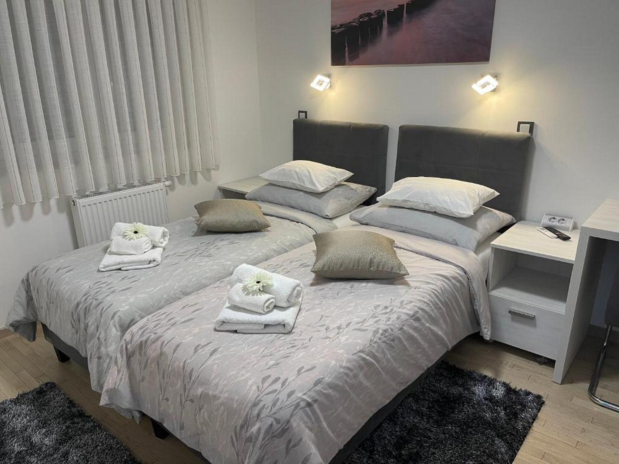 A modern bedroom with a large bed, two bedside tables, a nightstand, and a wall-mounted light fixture.
