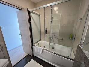 A modern bathroom with a glass-enclosed shower, a bathtub, and a door leading to an outdoor area.