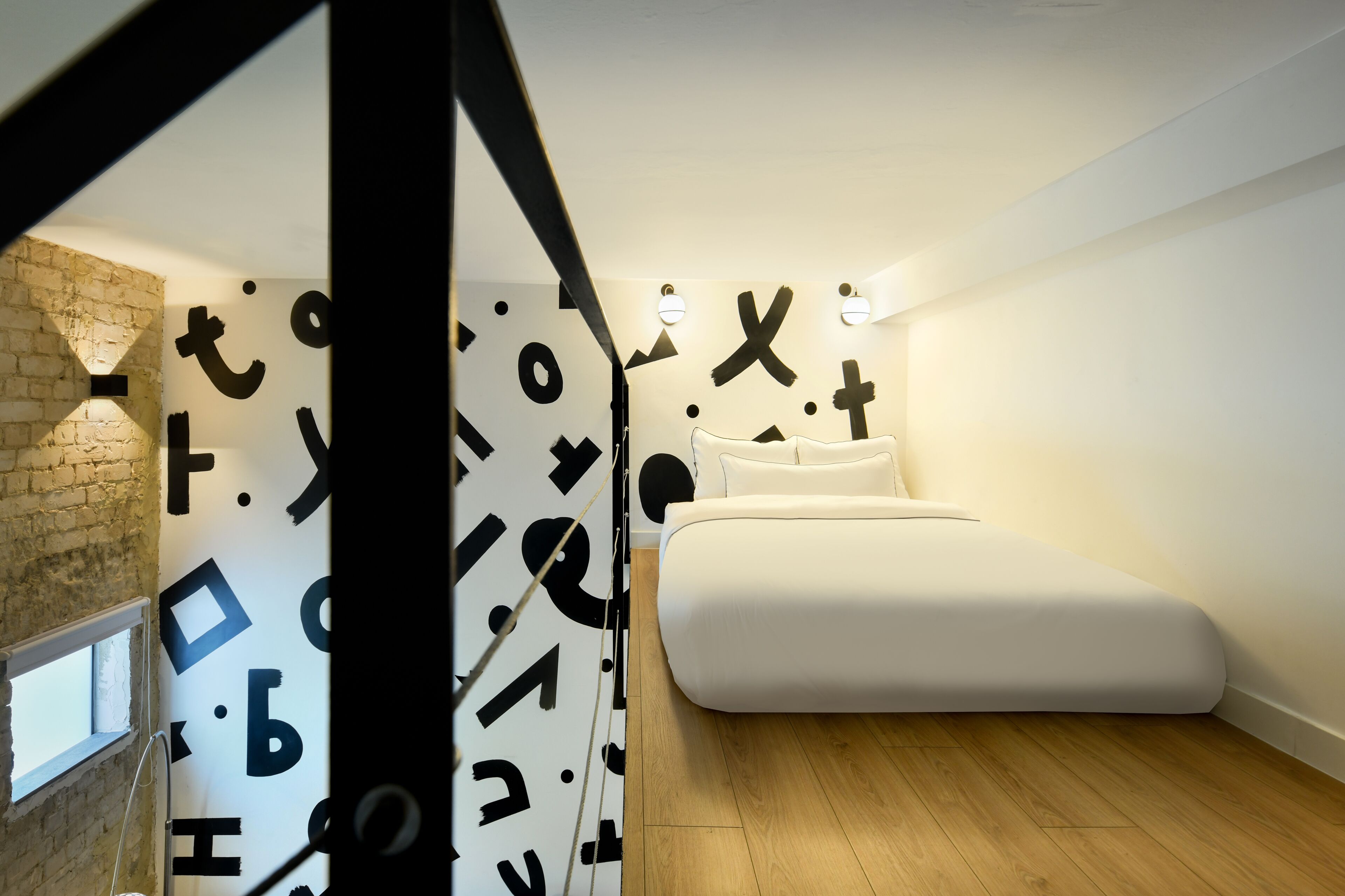 Een moderne slaapkamer met een minimalistisch design, met een bed, een bakstenen muur en abstracte wanddecoratie.