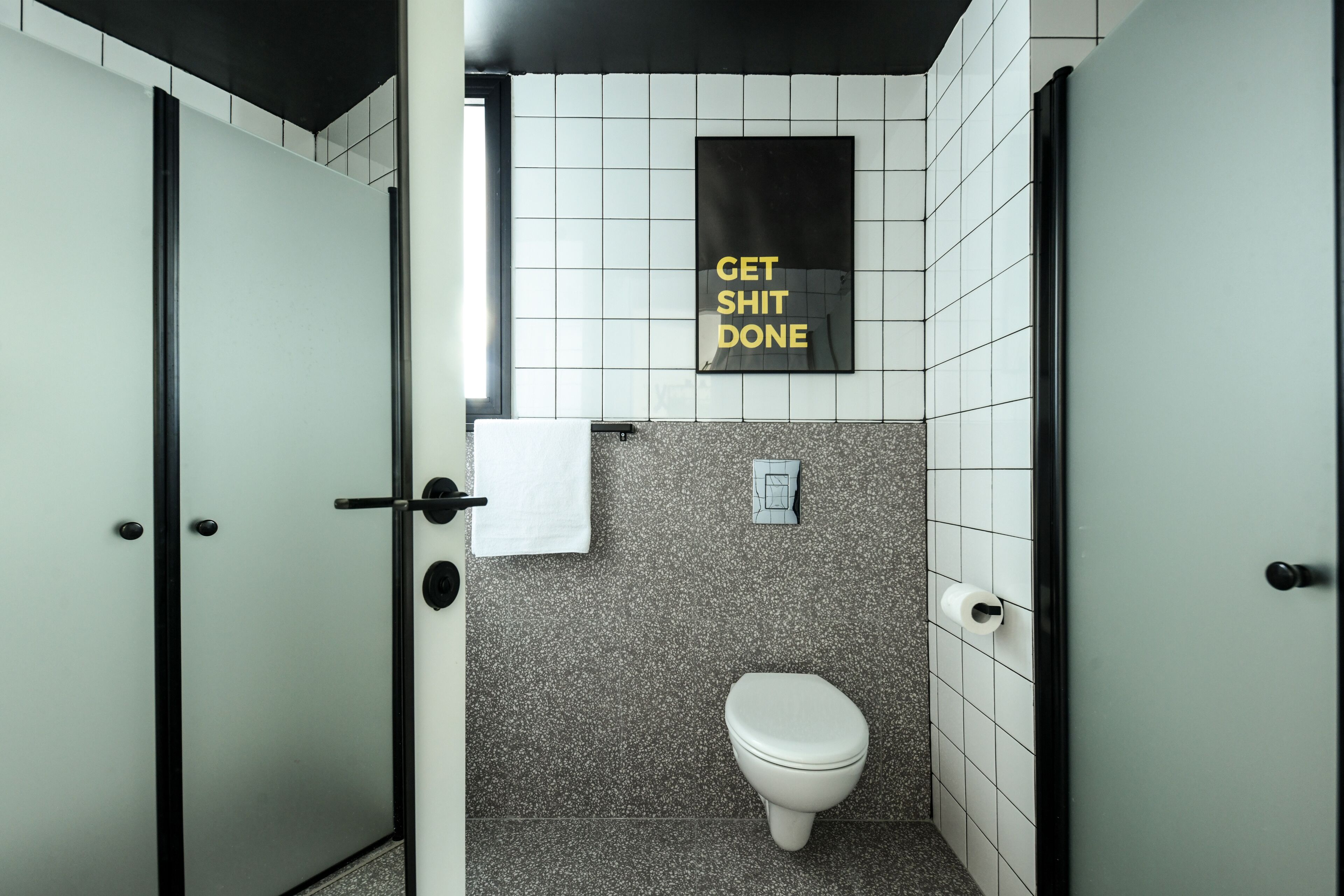 Uma casa de banho moderna com sanita, suporte para toalhas e um cartaz motivacional na parede.