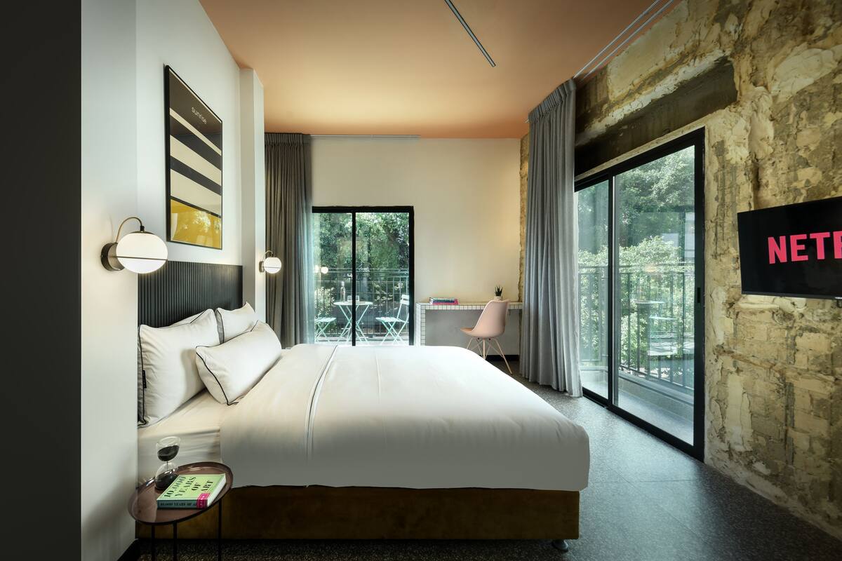 A modern hotel room with a large bed, a desk, and a view of the outdoors.
