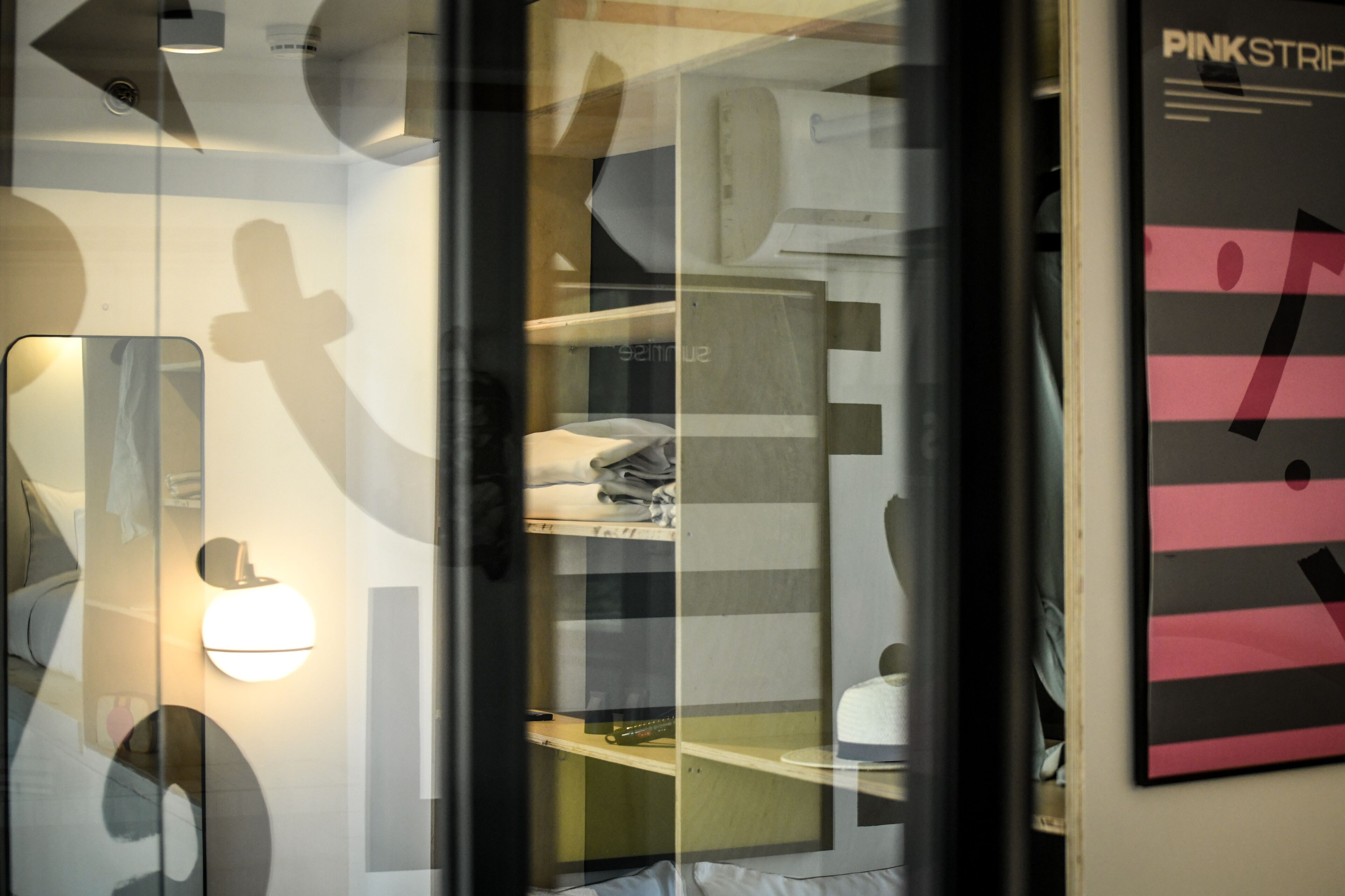 A modern hotel room with a glass partition, a bed, a nightstand, and a poster on the wall.