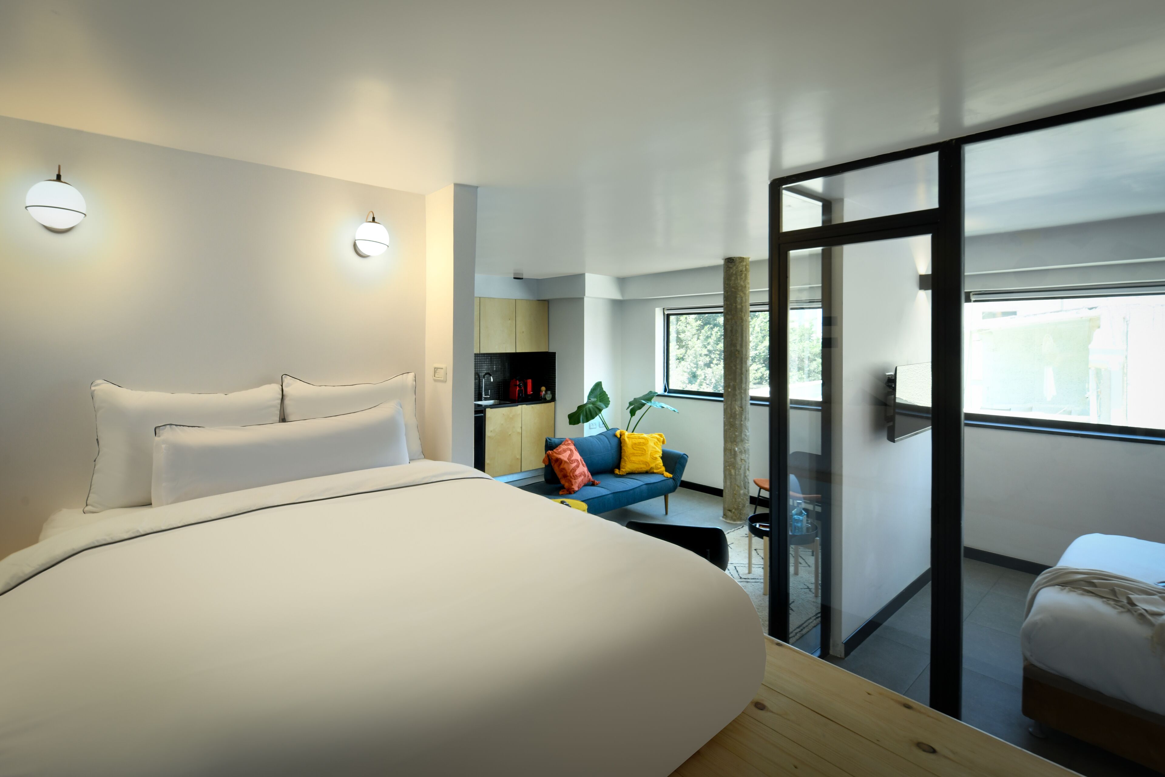 Una habitación de hotel moderna con una cama grande, un pequeño sofá, un área de comedor y un balcón con vistas.