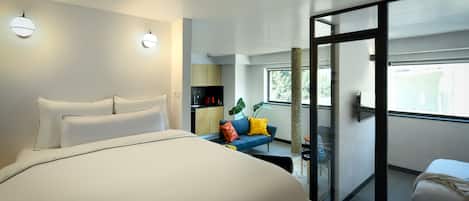 Una habitación de hotel moderna con una cama grande, un pequeño sofá, un área de comedor y un balcón con vistas.