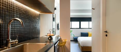 A modern hotel room with a kitchen area, a bed, and a view of the outdoors.