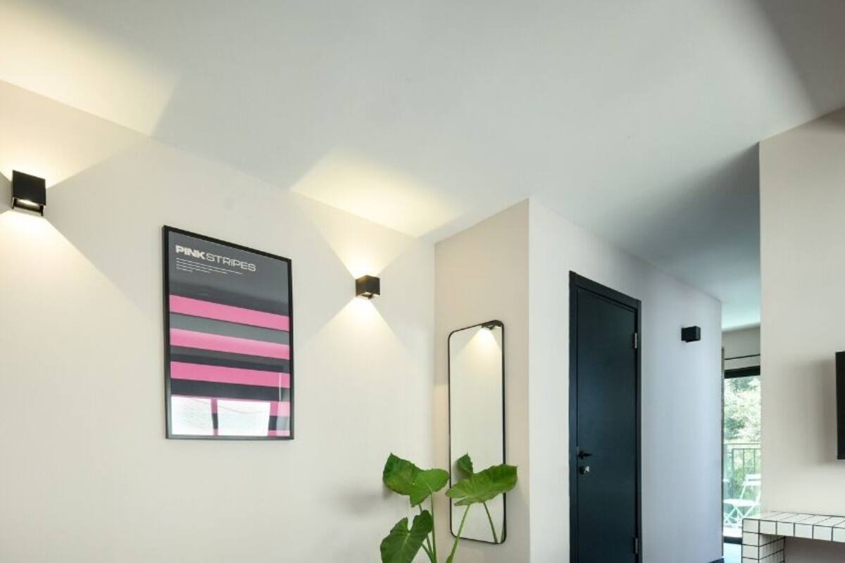 A modern bathroom with a large mirror, a wall-mounted light fixture, and a poster.