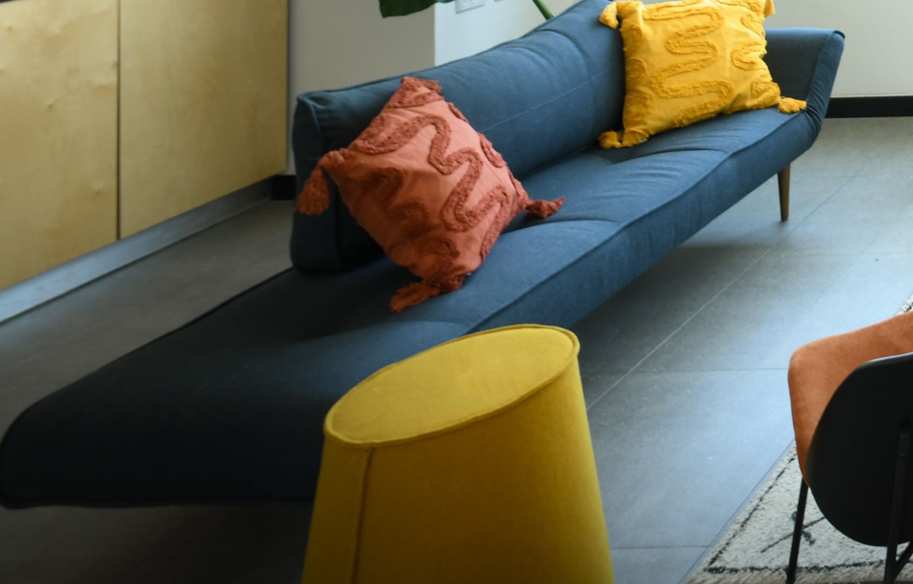 Un salon moderne avec un canapé bleu foncé, un pouf jaune et un coussin décoratif marron.