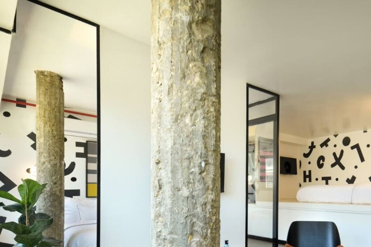 A modern room with a large mirror, a bed, a desk, and a plant.