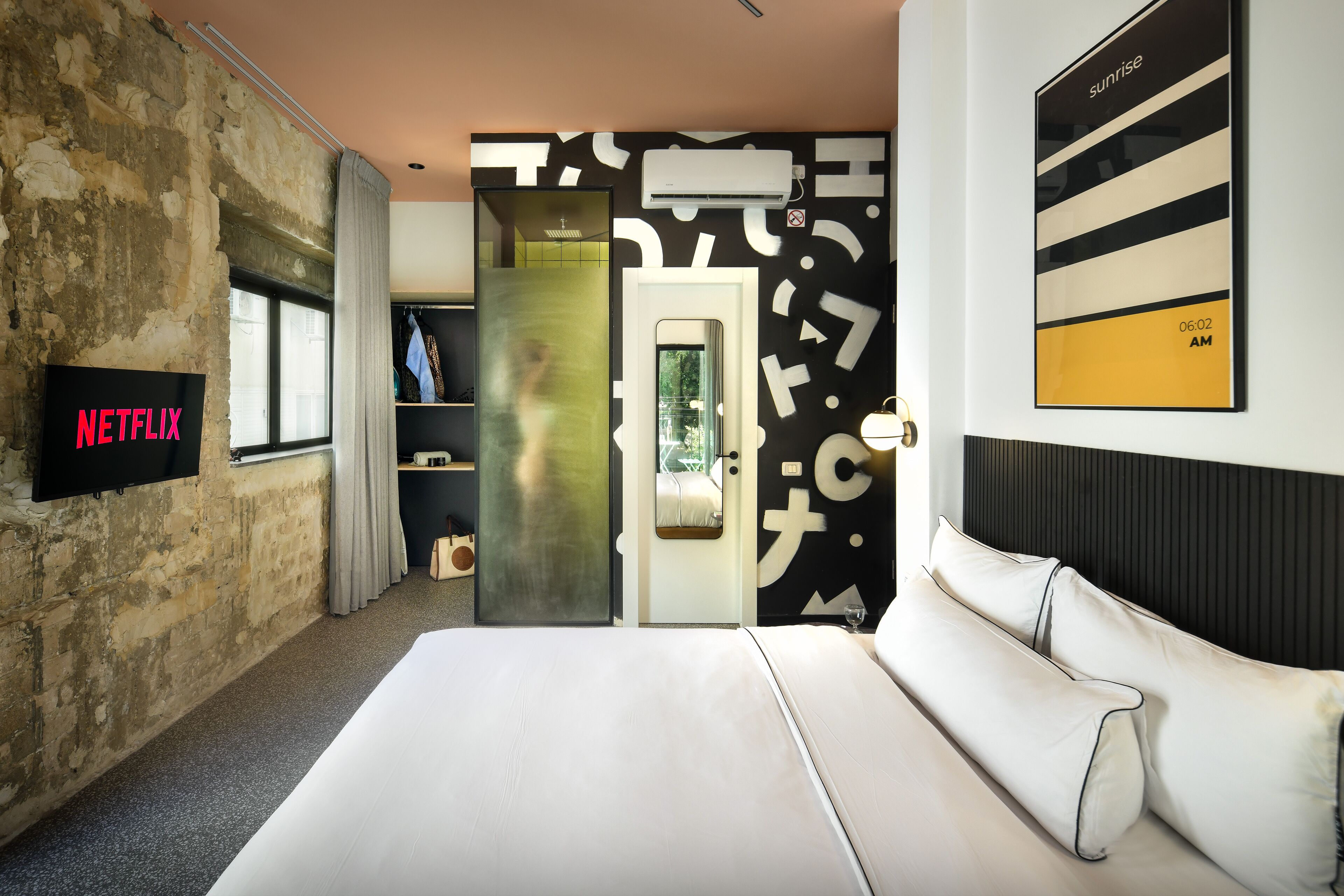 A modern hotel room with a large bed, a TV displaying 'NETFLIX', a wardrobe, and a wall with abstract patterns.