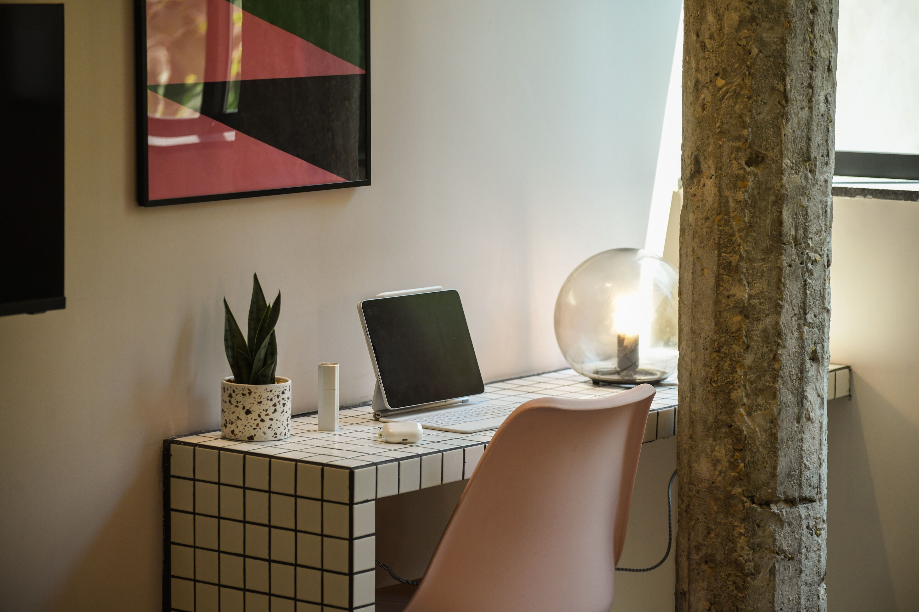 Ein moderner Arbeitsplatz mit einem Fliesen-Schreibtisch, einem Laptop, einer Topfpflanze und einer dekorativen Lampe.