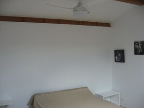 A bedroom with a bed, a ceiling fan, and two framed pictures on the wall.