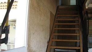 A wooden staircase in a building with a rough wall texture and a window on the left.
