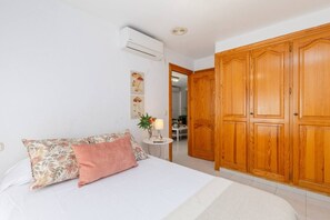 A bedroom with a bed, a nightstand, an air conditioning unit, and a wooden wardrobe.