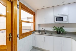 A kitchen with white cabinets, a stainless steel sink, a microwave, and a window with a wooden frame.