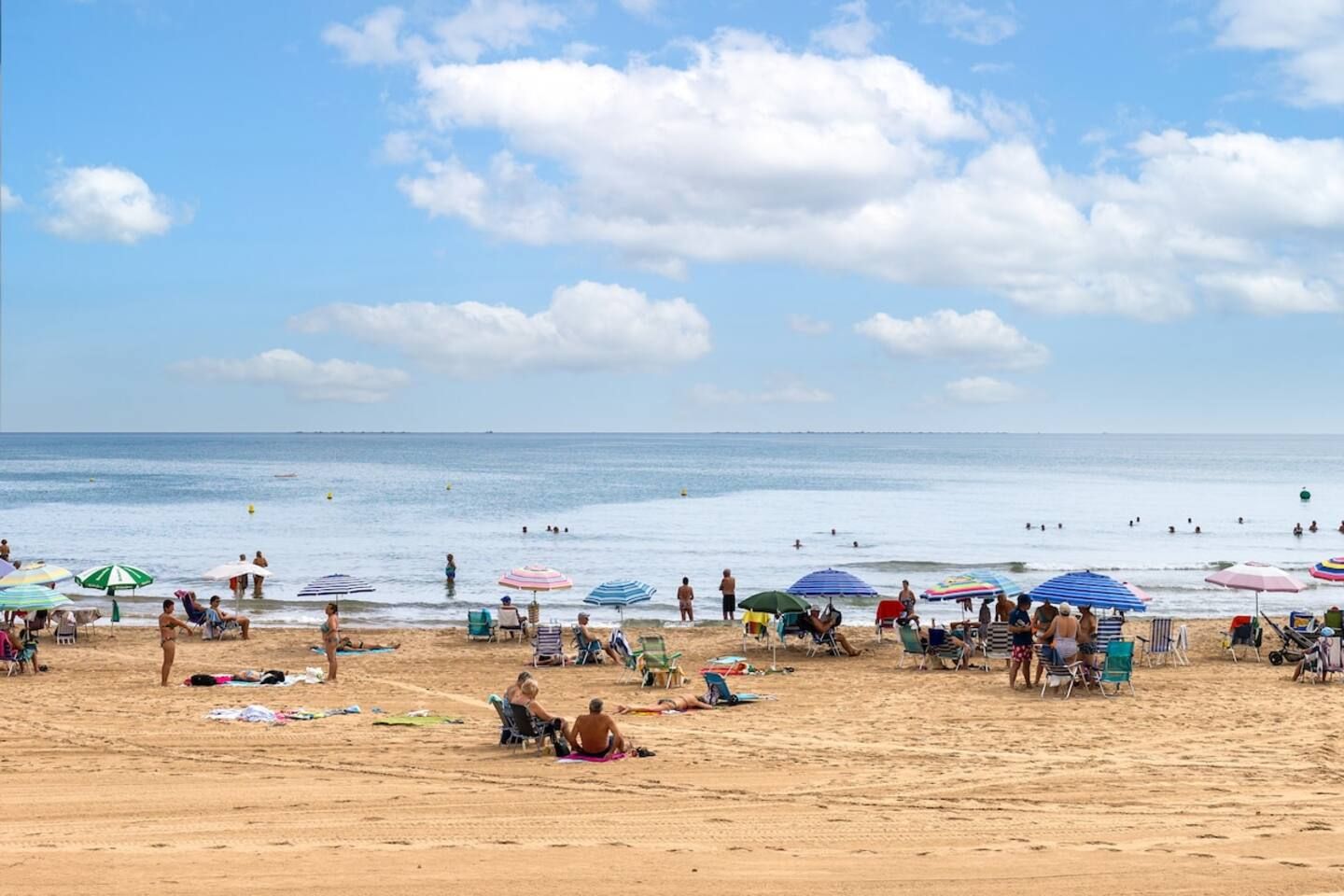 Une plage où l’on peut voir des gens bronzer et se baigner, avec des parasols et des chaises de plage.