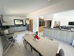 A modern kitchen with a central island, a dining area with a table and chairs, and a living area with a sofa and TV. - Villa in Porto vecchio, private pool, 5 minutes from the beach (Porto-Vecchio)