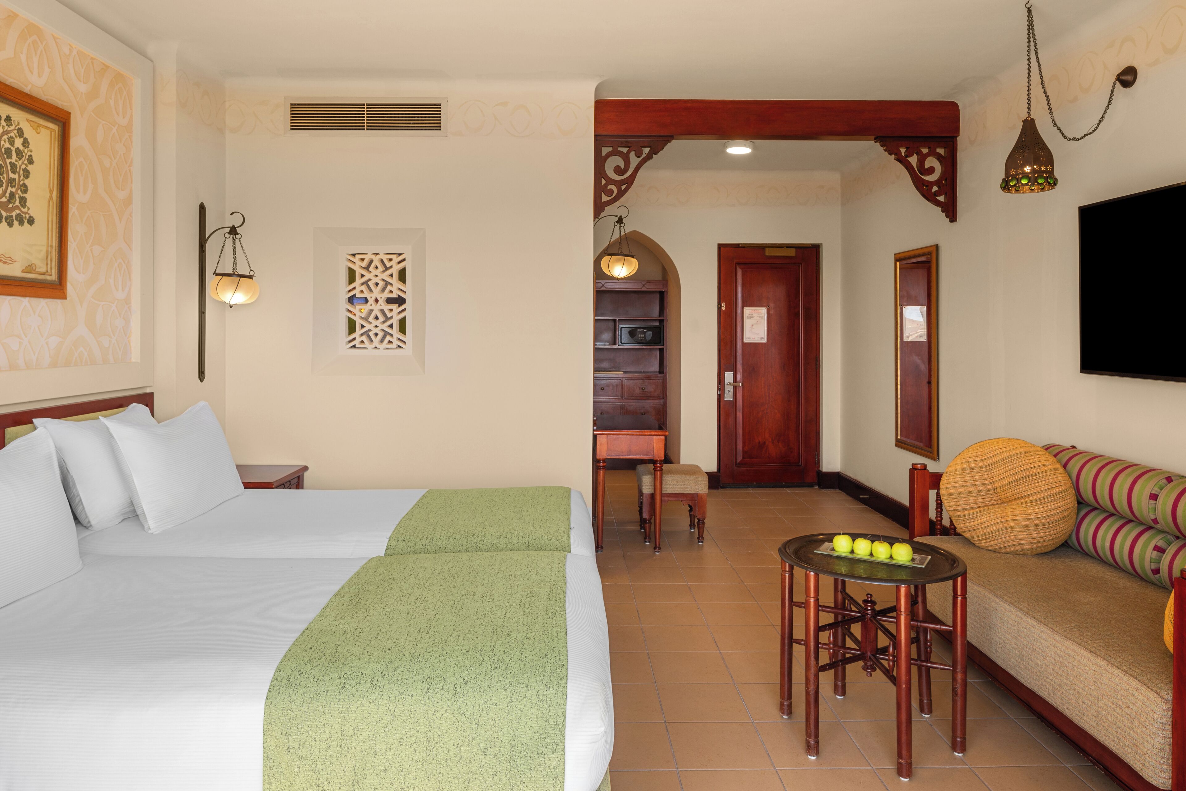 Habitación de hotel con una cama grande, una mesita con fruta, un sofá y un televisor.