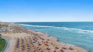 A beach with rows of sun loungers and umbrellas, a pier extending into the sea, and a clear sky.