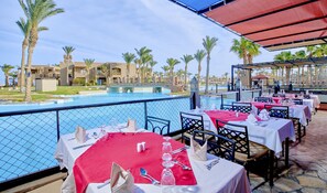 A dining area with tables set for a meal, overlooking a swimming pool and palm trees.
