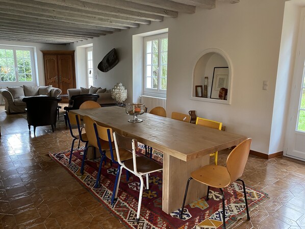 Uma sala de jantar espaçosa com uma longa mesa de madeira, várias cadeiras e um tapete estampado.