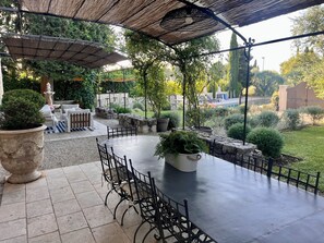 An outdoor patio with a round table and chairs, surrounded by potted plants and a stone wall.
