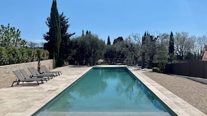 Piscina rectangular con borde de baldosas, rodeada de árboles y una valla.