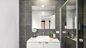 A modern bathroom with a white vanity, a mirror, and a glass shower enclosure. - Chatley's (Aireys Inlet)