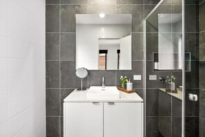 A modern bathroom with a white vanity, a mirror, and a glass shower enclosure. - Chatley's (Aireys Inlet)