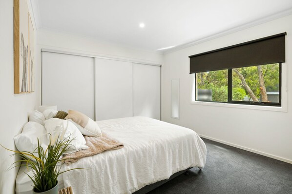 A bedroom with a bed, a window with a view of trees, and a plant on the floor.