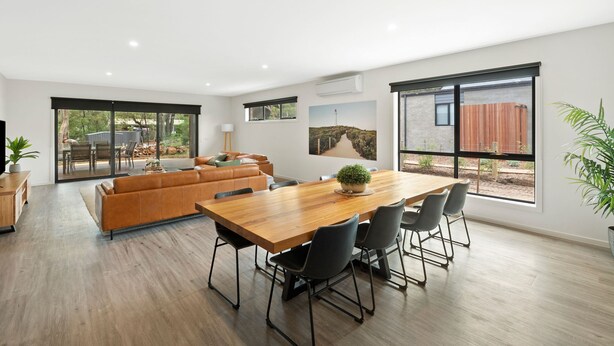 A modern living space with a wooden dining table, leather sofa, and large windows. - Chatley's (Aireys Inlet)