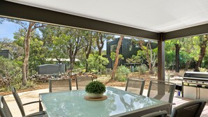 An outdoor patio with a glass table, chairs, and a grill. - Chatley's (Aireys Inlet)