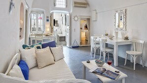 A spacious living area with a white sofa, a dining table, and a kitchen in the background. - Pyrgos 3-bed Villa, Sleeps 8, With Pool and Aircon (Santorini)