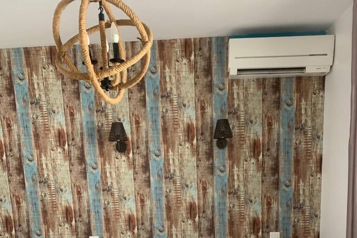 A hotel room with a bed, a chandelier, an air conditioning unit, and a wall with a wooden pattern.