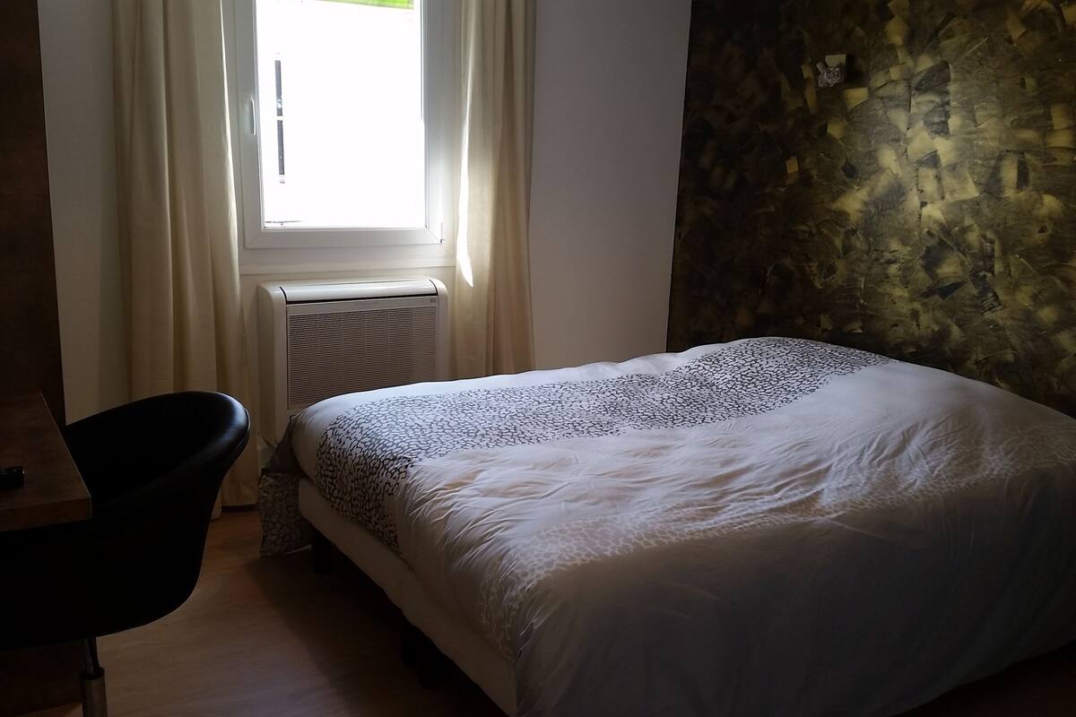 A bedroom with a bed, a chair, a window with curtains, and a radiator.